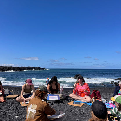 Group of people sitting on a black sand beach with ocean and blue sky in the background